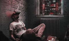 A man sitting alone on the floor against a brick wall, contained and quiet