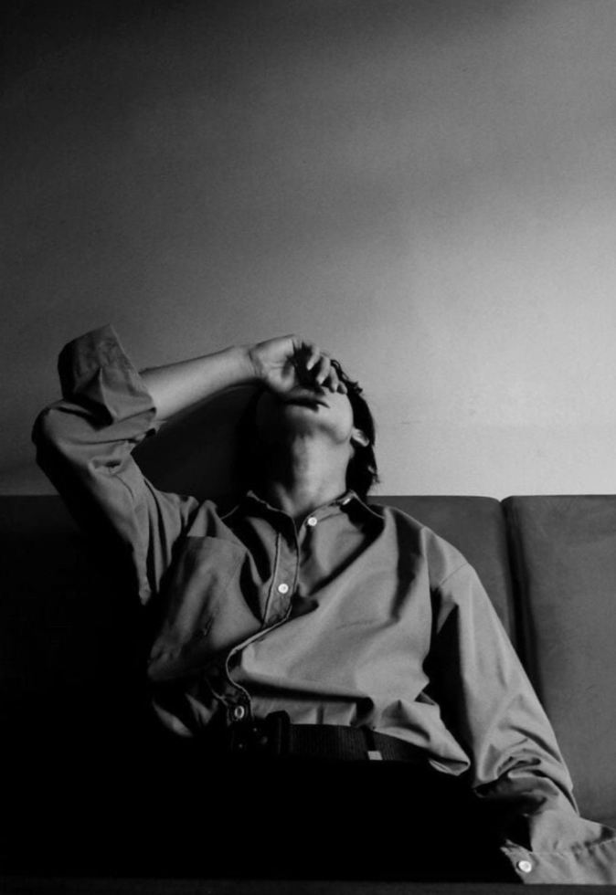 Man seated on a couch with hand covering his face, in a private moment of grief