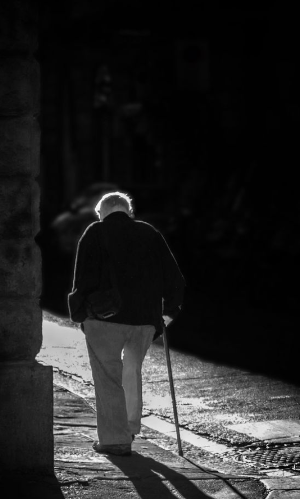 Elderly man walking with a cane, stepping into the sunlight